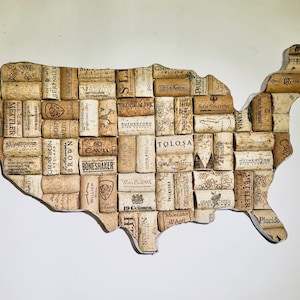 May include: A cork map of the United States of America. The map is made of wine corks with various winery names printed on them. The map is a light brown color.
