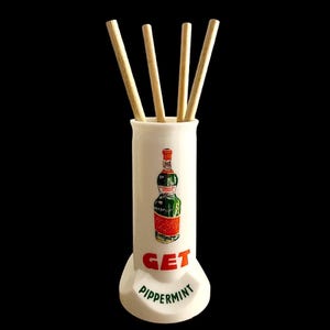 Può includere: Un portabastoncini in ceramica bianca con un'illustrazione in stile vintage di una bottiglia verde e rossa. Le parole "GET" e "Peppermint" sono stampate in rosso e verde. Quattro bastoncini di legno sono all'interno.