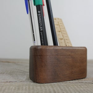 May include: A dark brown wooden desk organizer with rounded edges. It holds a blue, green, and black pen, and a wooden ruler.