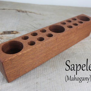 May include: A wooden pencil holder with multiple compartments for pencils, pens, and other writing utensils. The holder is made of sapele wood, also known as mahogany.
