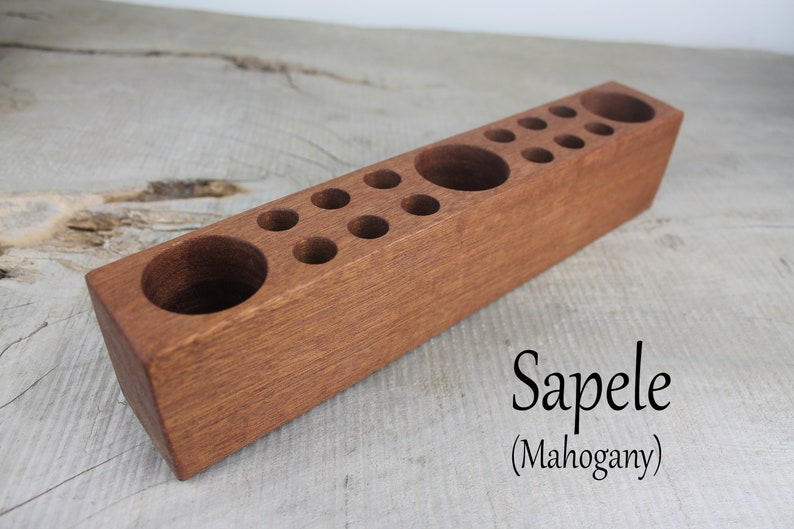 May include: A wooden pencil holder with multiple compartments for pencils, pens, and other writing utensils. The holder is made of sapele wood, also known as mahogany.