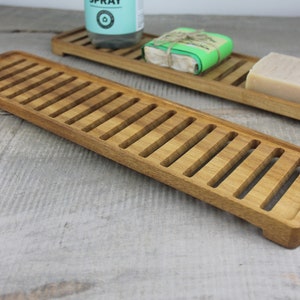 May include: Two wooden soap dishes with slatted bottoms. The dishes are made of natural wood and have a light brown color. The dishes are perfect for keeping soap dry and well-ventilated.