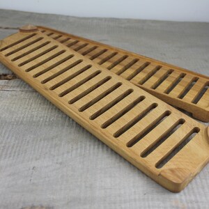 May include: Two wooden bread boards with a slatted design. The boards are made of light brown wood and are stacked on top of each other.