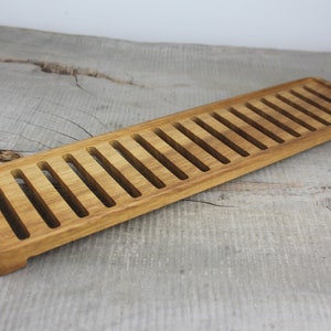 May include: A long, rectangular wooden tray with a series of evenly spaced slots cut into the surface. The tray is made of light brown wood and has a natural finish.