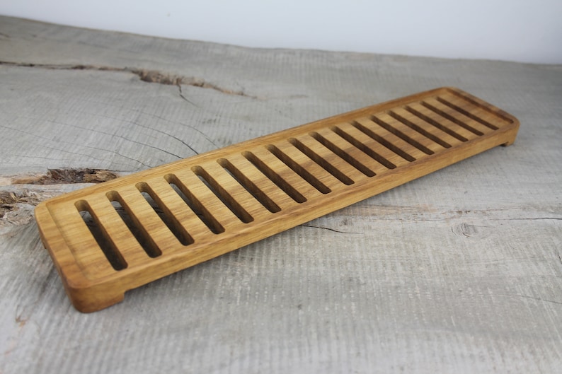 May include: A long, rectangular wooden tray with a series of evenly spaced slots cut into the surface. The tray is made of light brown wood and has a natural finish.