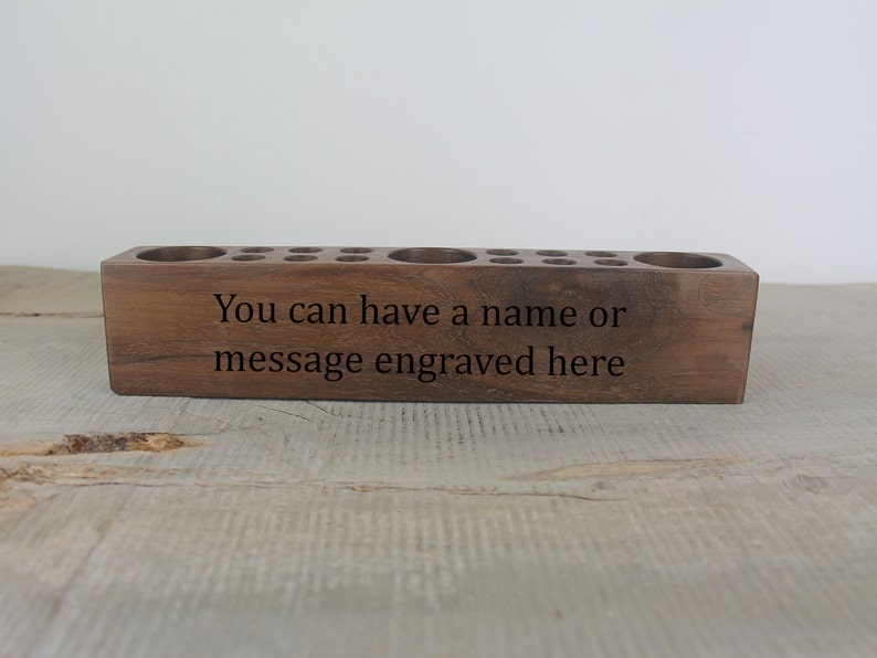 May include: A wooden pencil holder with multiple holes for pencils and a large space for other items. The holder is made of dark wood and has the text "You can have a name or message engraved here" on the front.