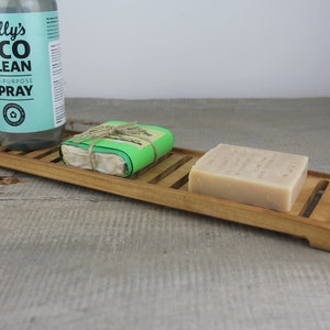 May include: A wooden soap dish with two bars of soap and a bottle of "Lilly's Eco Clean All-Purpose Spray".