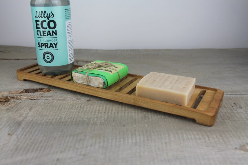 May include: A wooden soap dish with two bars of soap and a bottle of "Lilly's Eco Clean All-Purpose Spray".