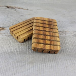 May include: Two wooden soap dishes with a slatted design. The dishes are made of light brown wood and are stacked on top of each other.