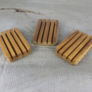 May include: Three wooden soap dishes with grooved ridges. The dishes are made of light brown wood and are arranged in a row on a gray wooden surface.