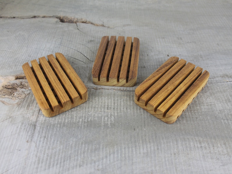 May include: Three wooden soap dishes with grooved ridges. The dishes are made of light brown wood and are arranged in a row on a gray wooden surface.