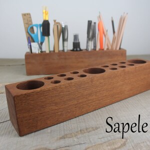 May include: A wooden pencil holder with multiple compartments for organizing pencils, pens, and other writing utensils. The holder is made of sapele wood and has a rich brown color.