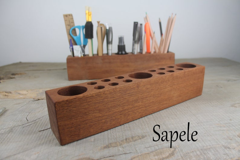 May include: A wooden pencil holder with multiple compartments for organizing pencils, pens, and other writing utensils. The holder is made of sapele wood and has a rich brown color.