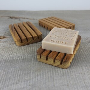 May include: Three wooden soap dishes with a bar of soap on one of them. The soap is beige and has text on it that reads "Mayfair Travel, Glycerine Body Wash, Palm Free, Handmade, 100g 3.5oz".