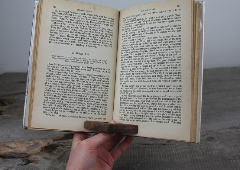 May include: An open book with a brown wooden bookmark. The book is titled "The Dog Crusoe" and the chapter is titled "Chapter XVI". The text on the page discusses the importance of listening to advice and the story of Dick Varley.