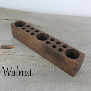 May include: A wooden organizer with multiple round holes for storing small items. The organizer is made of walnut wood and has a natural finish.
