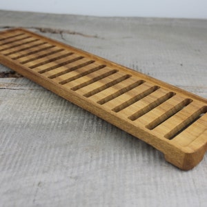 May include: A long, rectangular wooden tray with a series of evenly spaced slots cut into the top surface. The tray is made of light brown wood and has a slightly rounded edge.