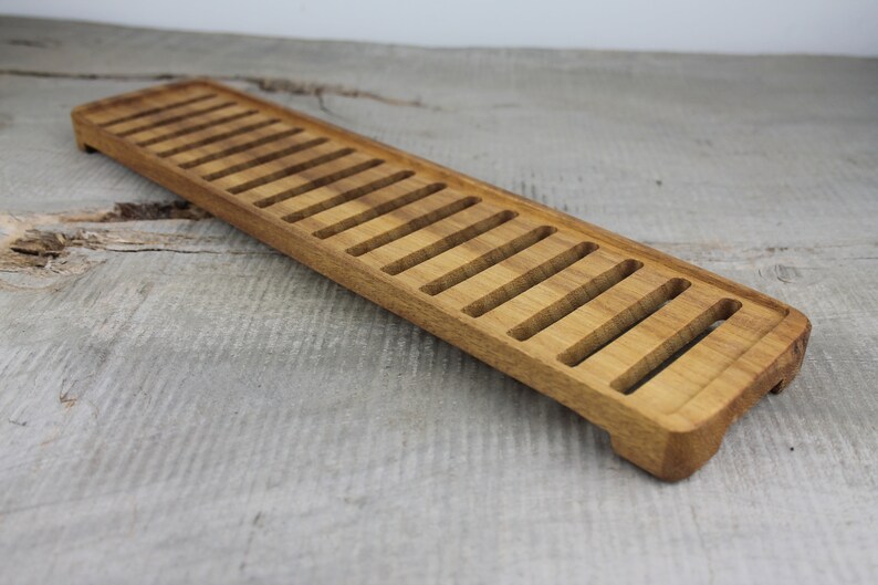 May include: A long, rectangular wooden tray with a series of evenly spaced slots cut into the top surface. The tray is made of light brown wood and has a slightly rounded edge.