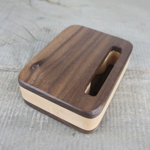 Puede incluir: Un soporte de tel&eacute;fono de madera hecho de nogal y arce. El soporte tiene un hueco para un tel&eacute;fono y un acabado de madera natural.