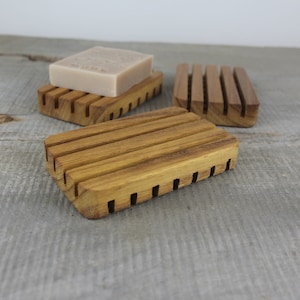 May include: Three wooden soap dishes with a slatted design. The dishes are made of natural wood and have a light brown color.
