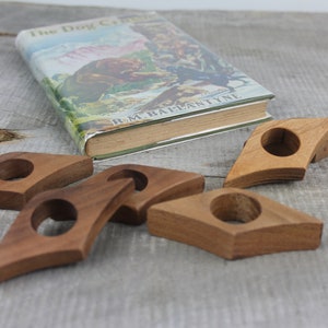 May include: Five wooden bookends in the shape of a diamond with a rounded hole in the center. The bookends are a light brown color and are arranged on a wooden surface.