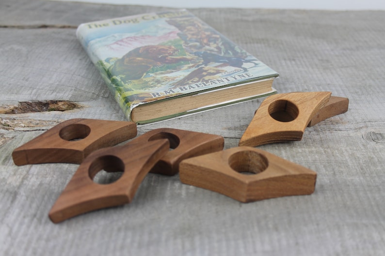 May include: Five wooden bookends in the shape of a diamond with a rounded hole in the center. The bookends are a light brown color and are arranged on a wooden surface.