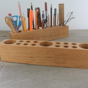 Può includere: Due portapenne in legno con più scomparti per penne, matite e altri strumenti di scrittura. I portapenne sono in legno marrone chiaro e hanno una finitura naturale.