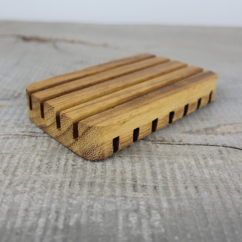 May include: A wooden soap dish with a grooved design to help drain water. The dish is made of natural wood and has a light brown color.