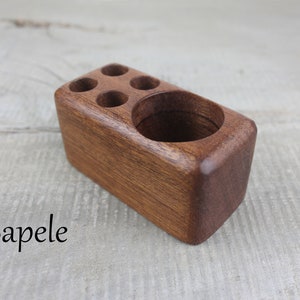 May include: A wooden pencil holder with five slots for pencils and a larger compartment for other items. The holder is made of sapele wood and has a natural finish.