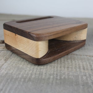 Puede incluir: Un soporte de tel&eacute;fono de madera con un dise&ntilde;o de madera de nogal y arce. El soporte tiene un recorte para un tel&eacute;fono y una base curva para amplificar el sonido.