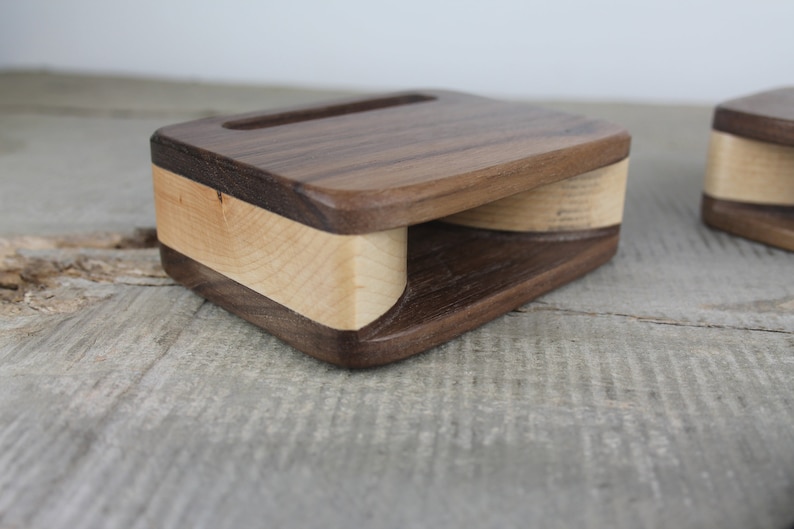 Puede incluir: Un soporte de tel&eacute;fono de madera con un dise&ntilde;o de madera de nogal y arce. El soporte tiene un recorte para un tel&eacute;fono y una base curva para amplificar el sonido.