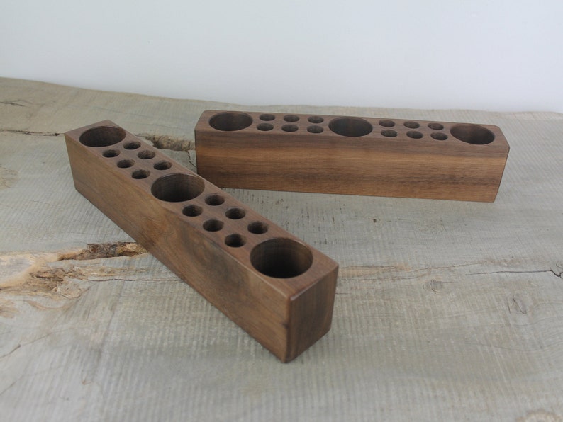 May include: Two wooden organizers with multiple round holes for storing small items. The organizers are made of dark brown wood and are sitting on a light brown wooden surface.