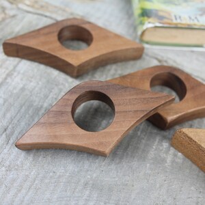 May include: Four wooden book page holders in the shape of a diamond with a rounded hole in the center. The holders are made of dark brown wood and are arranged on a light gray wooden surface.
