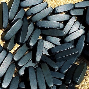 Peut inclure: Gros plan sur un tas de perles en bois rectangulaires noires. Les perles sont lisses et ont une finition mate.