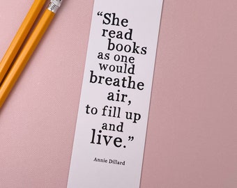 May include: A white bookmark with a black quote by Annie Dillard: "She read books as one would breathe air, to fill up and live."