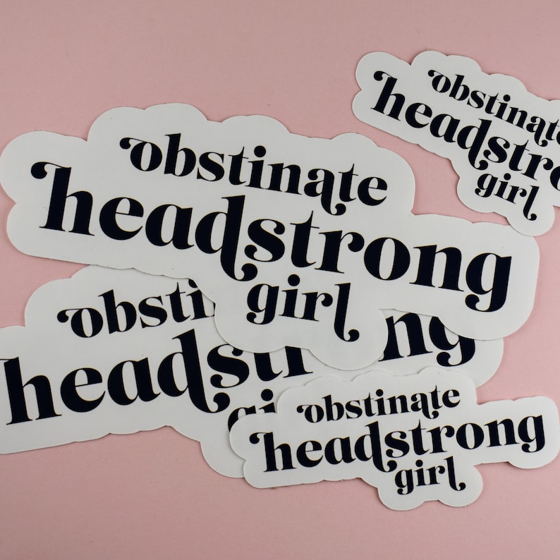 Op de afbeelding: Een set van vijf witte stickers met zwarte tekst. De tekst op de stickers luidt "obstinate headstrong girl".