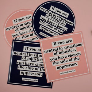 May include: Three pink and blue stickers with the quote "If you are neutral in situations of injustice, you have chosen the side of the oppressor." by Archbishop Desmond Tutu.