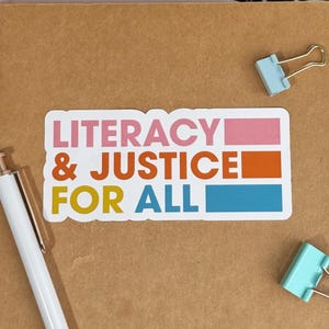 May include: A white sticker with the text "Literacy & Justice for All" in colorful block letters. The words "Literacy" and "Justice" are in a larger font size than "for All". The sticker has a pink, orange, and blue stripe behind the text.