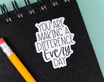 May include: A white sticker with black text that reads "You are making a difference every day" on a black notebook with a spiral binding.