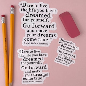 Op de afbeelding: Twee witte stickers met zwarte tekst op een roze achtergrond. De tekst op de stickers luidt "Durf te leven het leven waarvan je hebt gedroomd voor jezelf. Ga vooruit en maak je dromen waar." De tekst wordt toegeschreven aan Ralph Waldo Emerson.