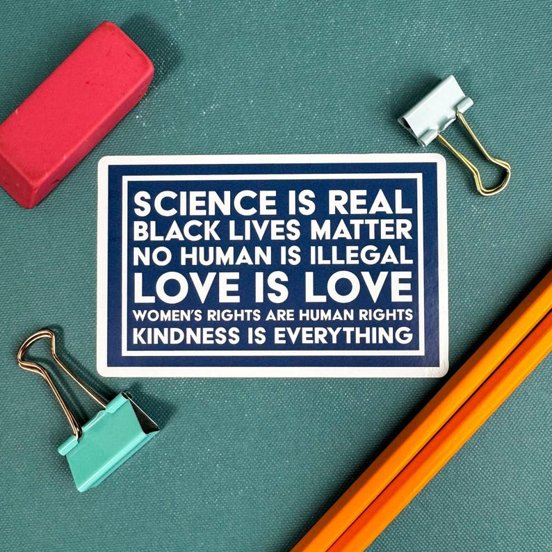 May include: A blue and white sign with the text "SCIENCE IS REAL, BLACK LIVES MATTER, NO HUMAN IS ILLEGAL, LOVE IS LOVE, WOMEN'S RIGHTS ARE HUMAN RIGHTS, KINDNESS IS EVERYTHING".