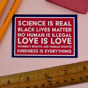 May include: A red and blue sticker with the text "SCIENCE IS REAL, BLACK LIVES MATTER, NO HUMAN IS ILLEGAL, LOVE IS LOVE, WOMEN'S RIGHTS ARE HUMAN RIGHTS, KINDNESS IS EVERYTHING."