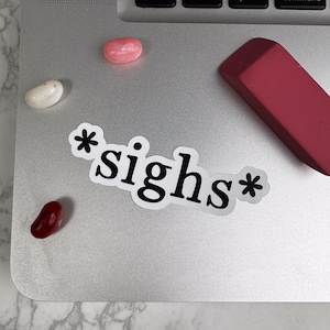 May include: A white sticker with the text "*sighs*" on a silver laptop with a pink and white candy and a red eraser.