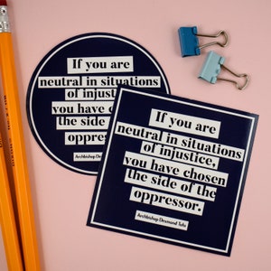 May include: Two blue and white stickers with a quote by Archbishop Desmond Tutu. The quote reads, "If you are neutral in situations of injustice, you have chosen the side of the oppressor."