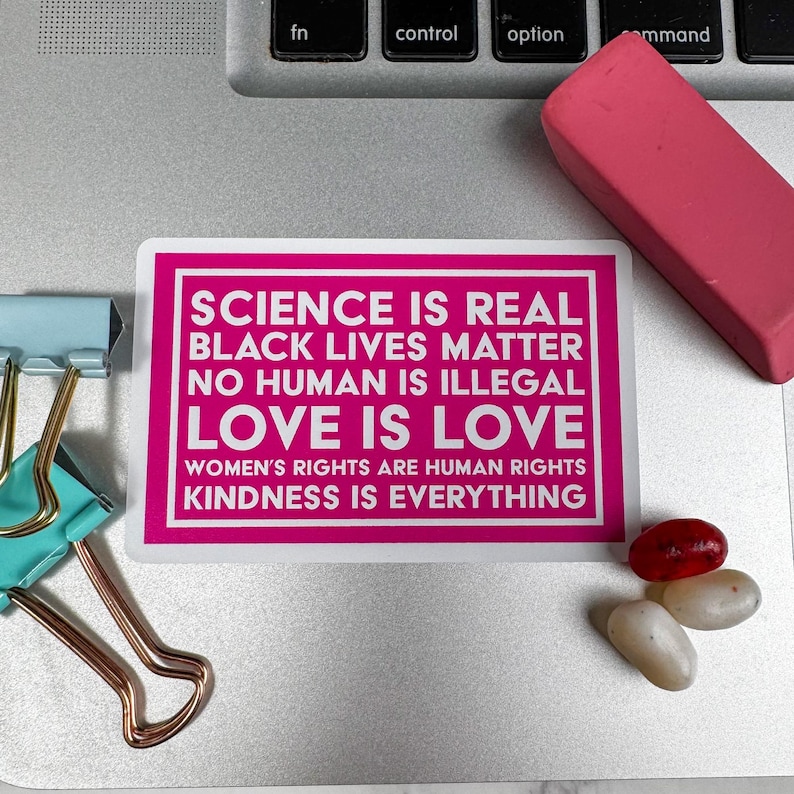 May include: A pink sticker with white text that reads "Science is real, Black Lives Matter, No Human is Illegal, Love is Love, Women's Rights are Human Rights, Kindness is Everything."