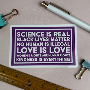 May include: A purple sticker with white text that reads "Science is real, Black lives matter, No human is illegal, Love is love, Women's rights are human rights, Kindness is everything."