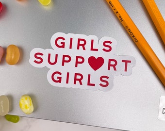 Op de afbeelding: Witte sticker met de tekst "Girls Support Girls" in rode letters met een rood hart in het midden van het woord "Support".
