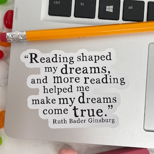 May include: A white sticker with a black quote by Ruth Bader Ginsburg: "Reading shaped my dreams, and more reading helped me make my dreams come true."
