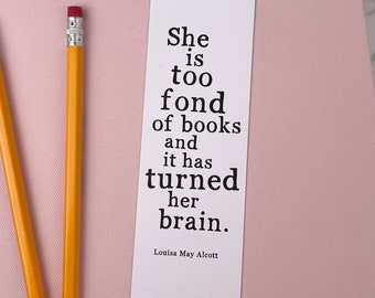 May include: A white bookmark with black text that reads "She is too fond of books and it has turned her brain."  The text is attributed to Louisa May Alcott.