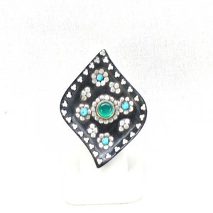 May include: A black and silver ring with a green and turquoise stone design. The ring is set in a diamond shape and has a unique, intricate design.
